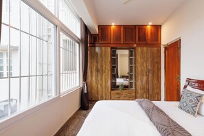 A bedroom with a large window, wooden wardrobe, and a bed with a patterned pillow. - The Honeywood3bhkindiranagarnr Itpl30min MG Rd (Bengaluru)