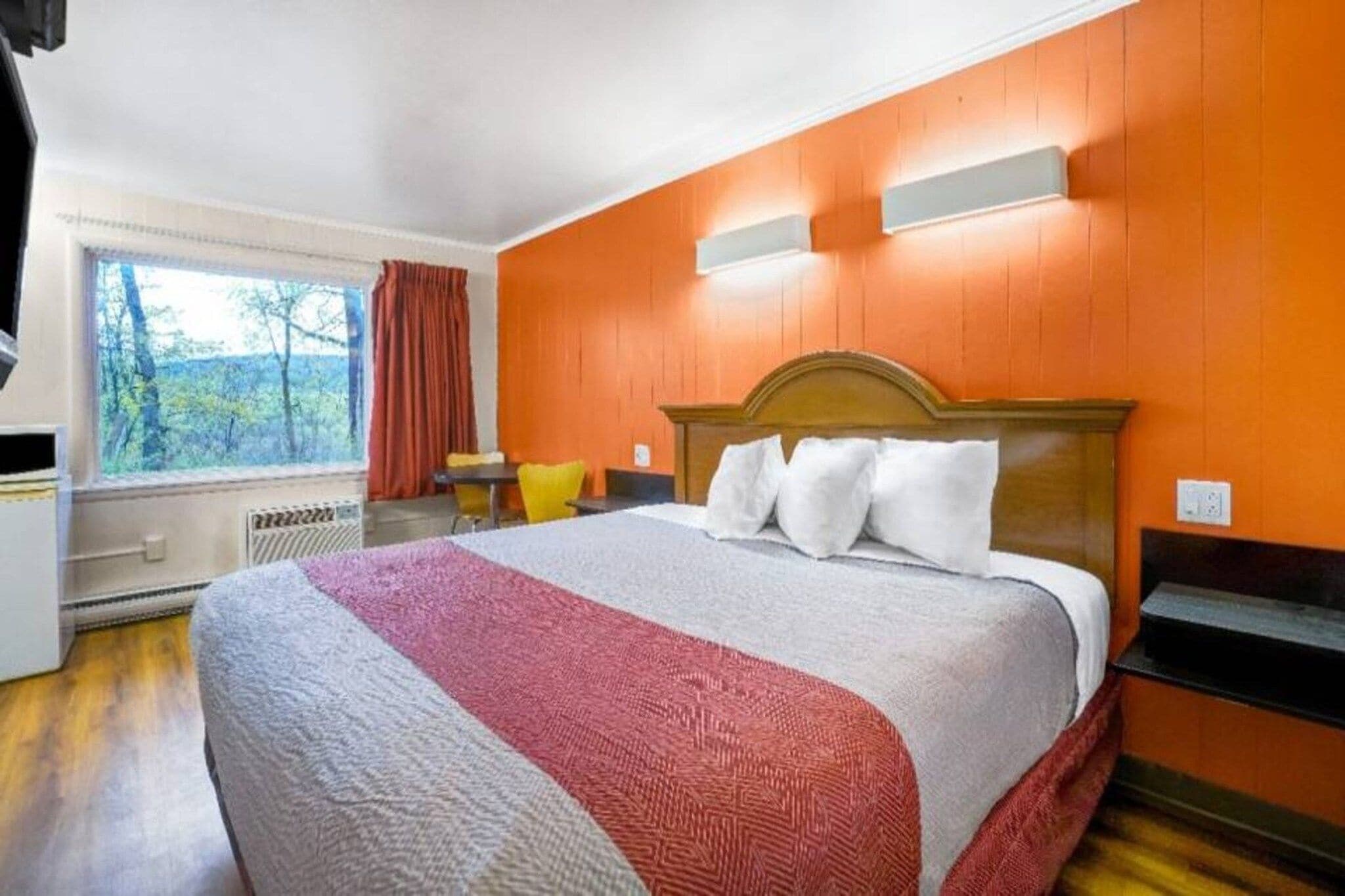 A hotel room with a large bed, a window with curtains, a small table, and a chair.