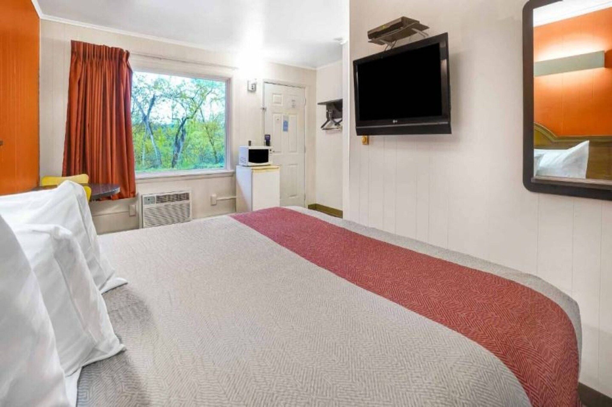 A hotel room with a bed, a television, a desk, and a window with curtains.