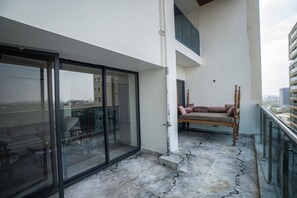 Un balcon doté d’une porte vitrée, d’un banc rembourré et offrant une vue sur le paysage urbain.