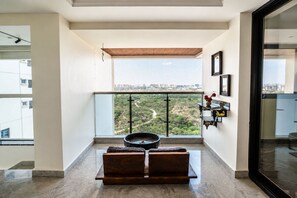 Ein Balkon mit Blick auf eine Stadtlandschaft, ein runder Tisch mit Kissen und ein Regal mit dekorativen Gegenständen.