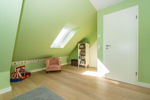 Habitació amb sostre inclinat, un lucernari, una biblioteca, una cadira i una porta.