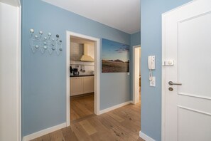 A hallway with a kitchen visible through an open door, a painting on the wall, and a phone on the wall. - Casa Karline - Casa Karline – Relaxed Living with a View of Sylt’s Greenery (Sylt)