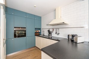 A kitchen with teal cabinets, a black countertop, and white tiled backsplash. - Casa Karline - Casa Karline – Relaxed Living with a View of Sylt’s Greenery (Sylt)