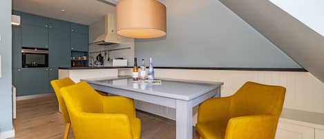 A modern kitchen with a central island, yellow chairs, and a hanging light fixture.