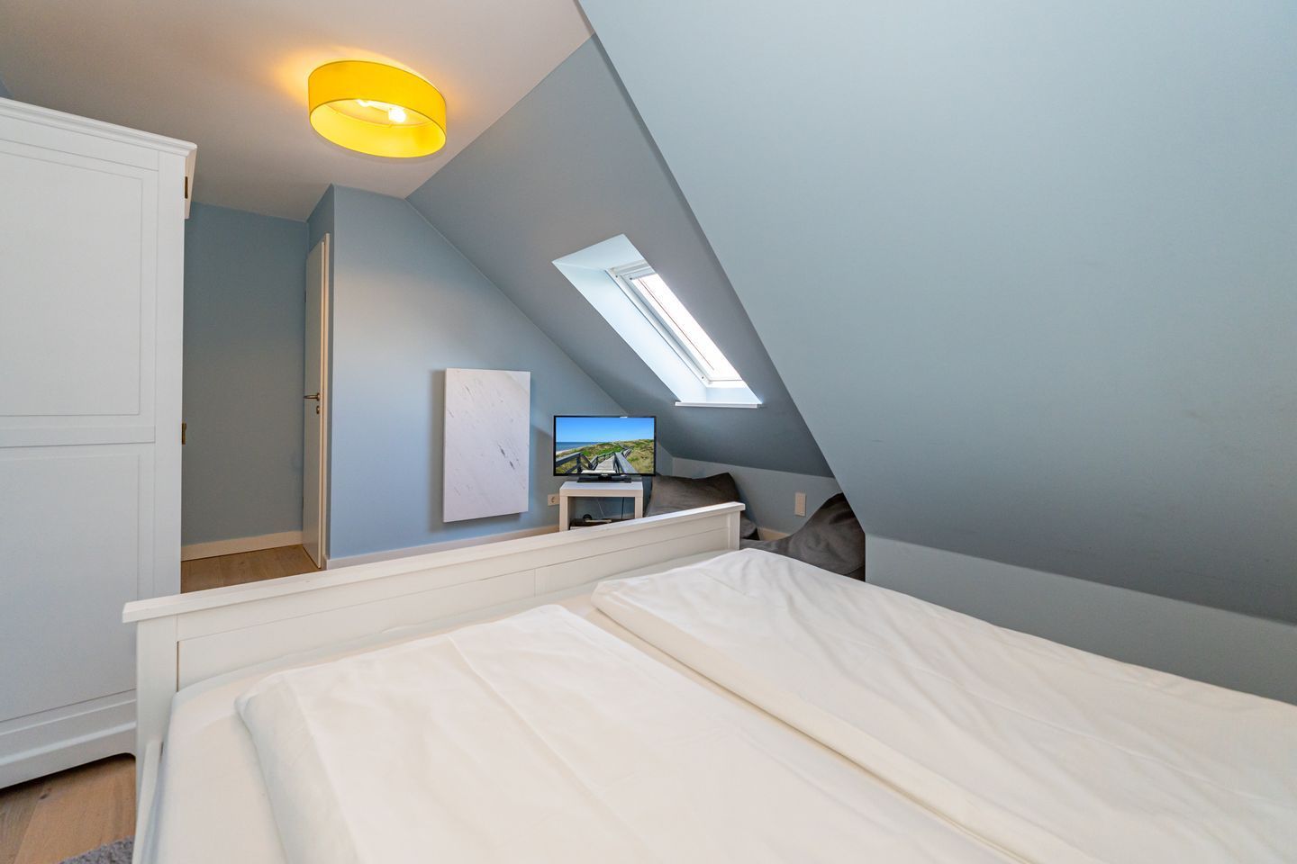 Een slaapkamer met een schuine kap, een dakraam, een bed, een televisie op een standaard en een kledingkast.