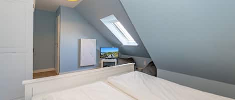 Een slaapkamer met een schuine kap, een dakraam, een bed, een televisie op een standaard en een kledingkast.