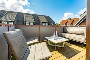 An outdoor balcony with two cushioned chairs and a small table, featuring a bottle and magazine. - Casa Karline - Casa Karline – Relaxed Living with a View of Sylt’s Greenery (Sylt)