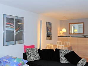 A modern living room with a black sofa, colorful cushions, a dining area with a white table and chairs, and a kitchen area with a wooden counter and a mirror. - Grifla 1-1 Appartement/Fewo, Dusche oder Bad, WC 2½-Zimmerwohnung by Interhome (Davos)