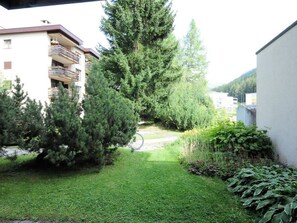 Un quartier résidentiel avec une pelouse verdoyante, un grand arbre à feuilles persistantes et un immeuble doté de balcons.