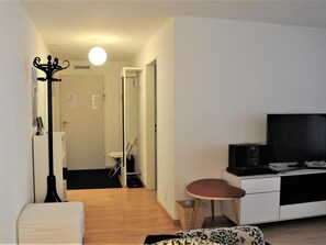 Een moderne woonkamer met een flatscreen televisie, een bank, een klein rond tafeltje en een kapstok.