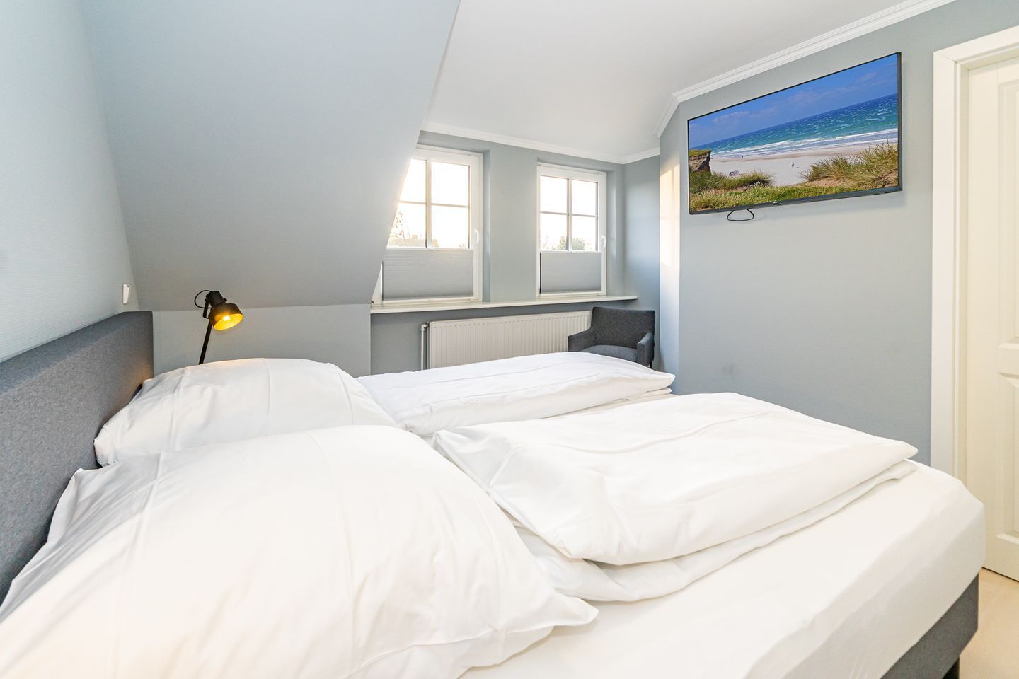 Ein Schlafzimmer mit zwei Betten, einem Fenster, einer Heizung, einem Sessel und einem Strandbild.