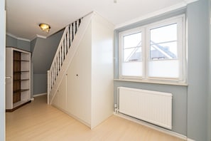 A staircase with a white railing, a radiator below a window, and a wooden bookshelf to the left. - Black-headed Gull - Black-headed Gull – a stylish island home with a fireplace and garden (Sylt)