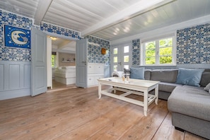 Ein Zimmer mit Holzboden, einem weißen Tisch, einem grauen Sofa und blauen Wänden mit Muster.
