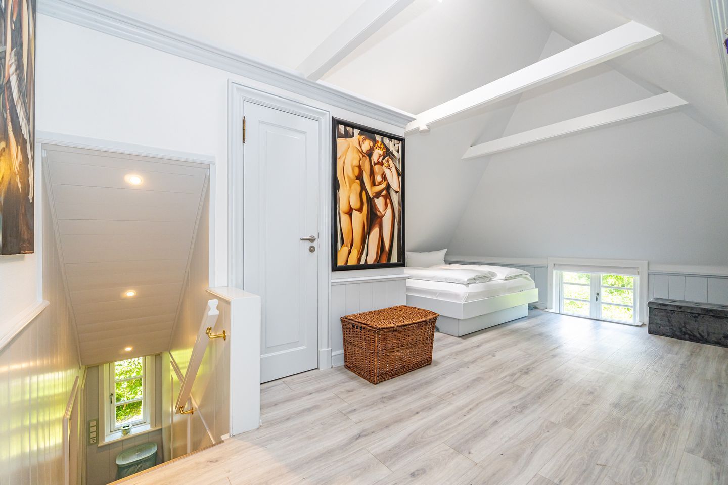 Une pièce spacieuse avec un plafond haut, un grand tableau, un lit et un escalier.
