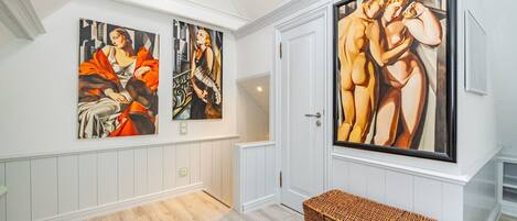 Un couloir avec trois grands tableaux accrochés au mur, un panier en osier et une porte blanche.