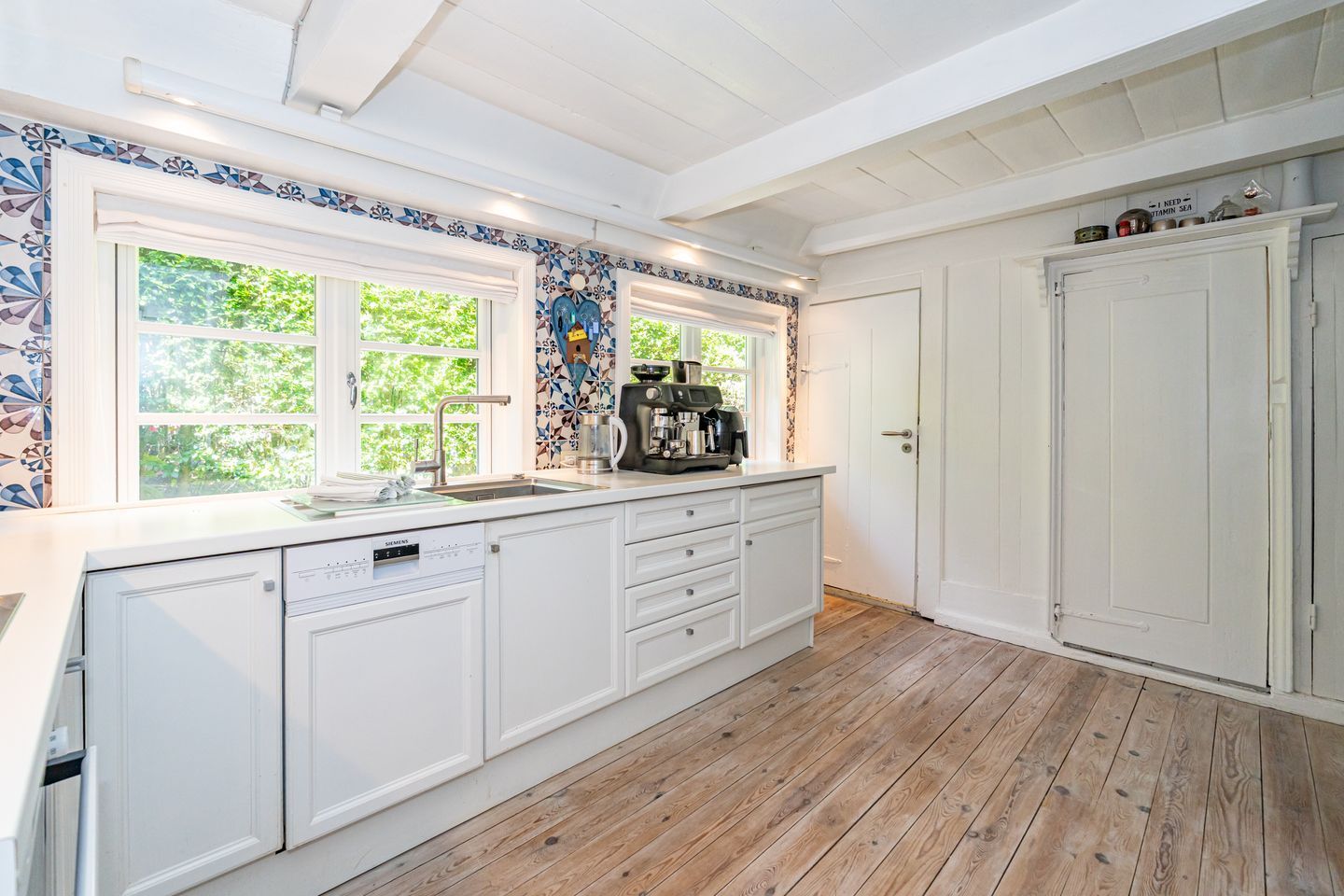 A kitchen with white cabinetry, a dishwasher, a coffee machine, and a window with a view of greenery.