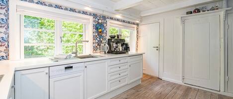 A kitchen with white cabinetry, a dishwasher, a coffee machine, and a window with a view of greenery.