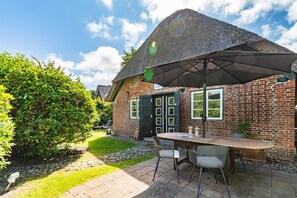 A brick house with a thatched roof, a patio with a table and chairs, and a well-maintained garden. - Kapitänshuis - Kapitänshuis – a Frisian island home full of character (Sylt)