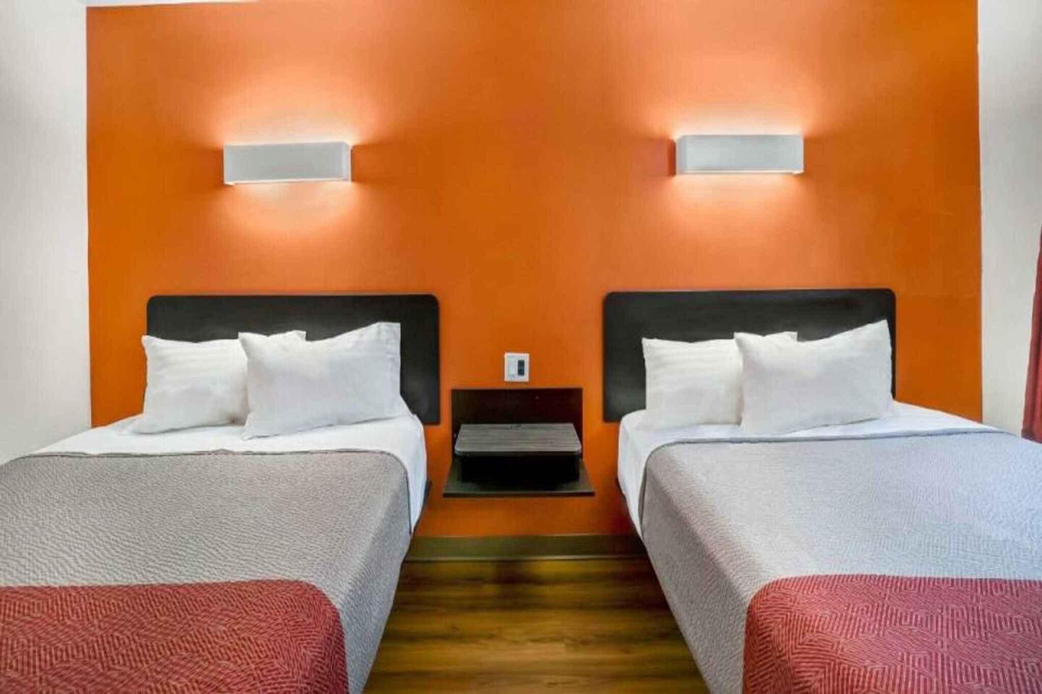 Une chambre d’hôtel avec deux lits, un plancher en bois et une table de chevet fixée au mur, placée entre les deux lits.