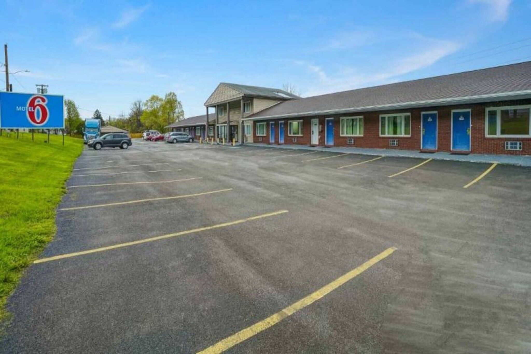 A motel with a large parking lot, a signboard, and a building with multiple doors.