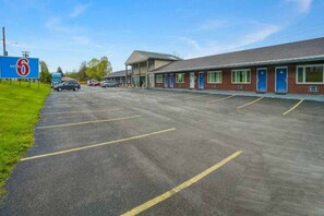 A motel with a large parking lot, a signboard, and a building with multiple doors.