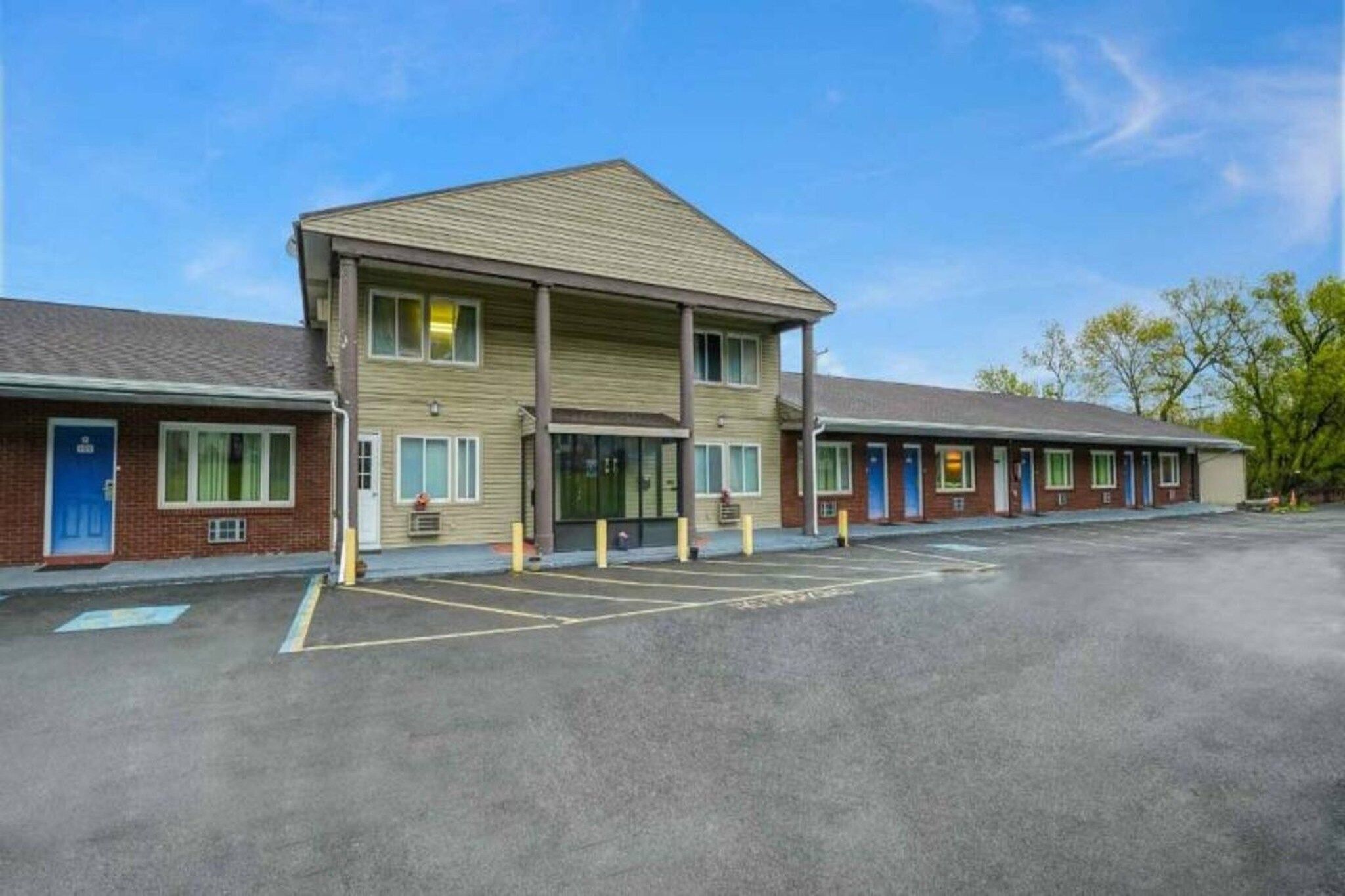 A motel with a central building and attached units, a parking lot, and a clear sky.