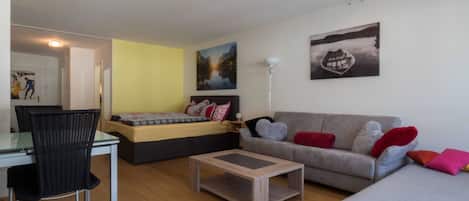 A modern living room with a sofa, a bed, a dining table, and a chair.