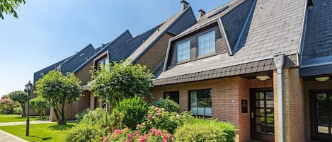 A row of modern houses with pitched roofs and brick exteriors, surrounded by well-maintained gardens and a clear sky.