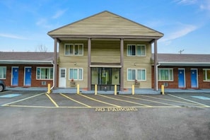 A motel with a central entrance, a parking lot with no parking signs, and a row of rooms on either side.
