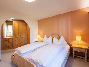 Ein Schlafzimmer mit einem Doppelbett, zwei Nachttischen mit Lampen, einem Holzschrank und einem Rundbogenfenster.