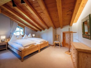 Une chambre avec un plafond en bois, un lit, une chaise, une commode et une fenêtre.