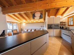 Eine moderne Küche mit einer zentralen Kochinsel, Holzbalkendecke und eingebauten Geräten.