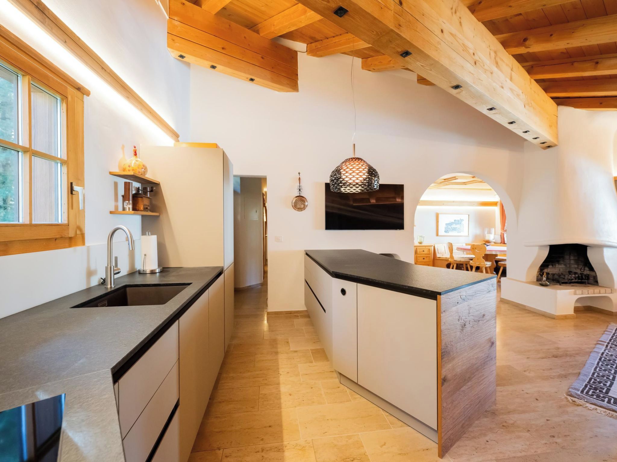 Una cocina moderna con vigas de madera, una isla integrada y una chimenea en la zona de estar.