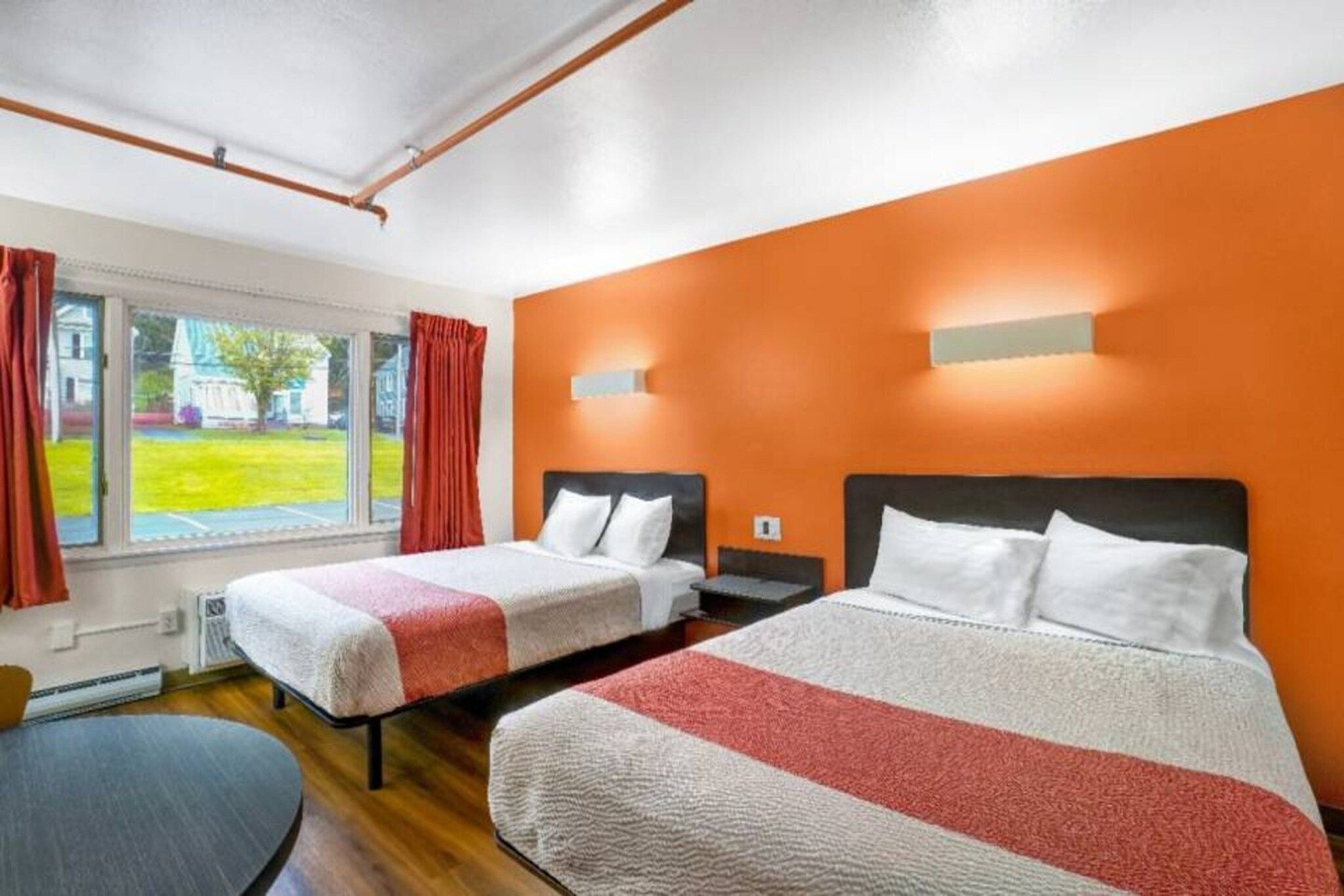 A hotel room with two beds, a window with curtains, and an orange wall.