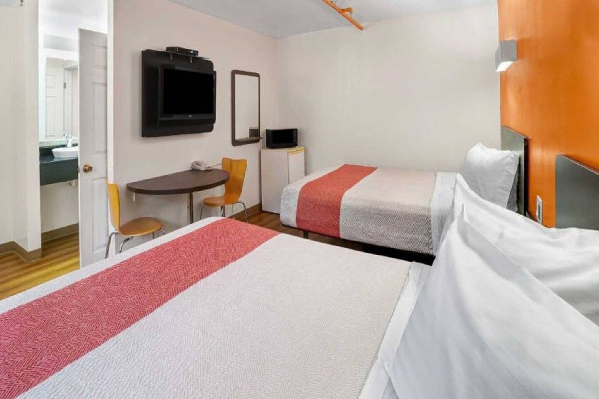 Habitació d'hotel amb dos llits, una taula de treball, una cadira, un televisor i un microones.