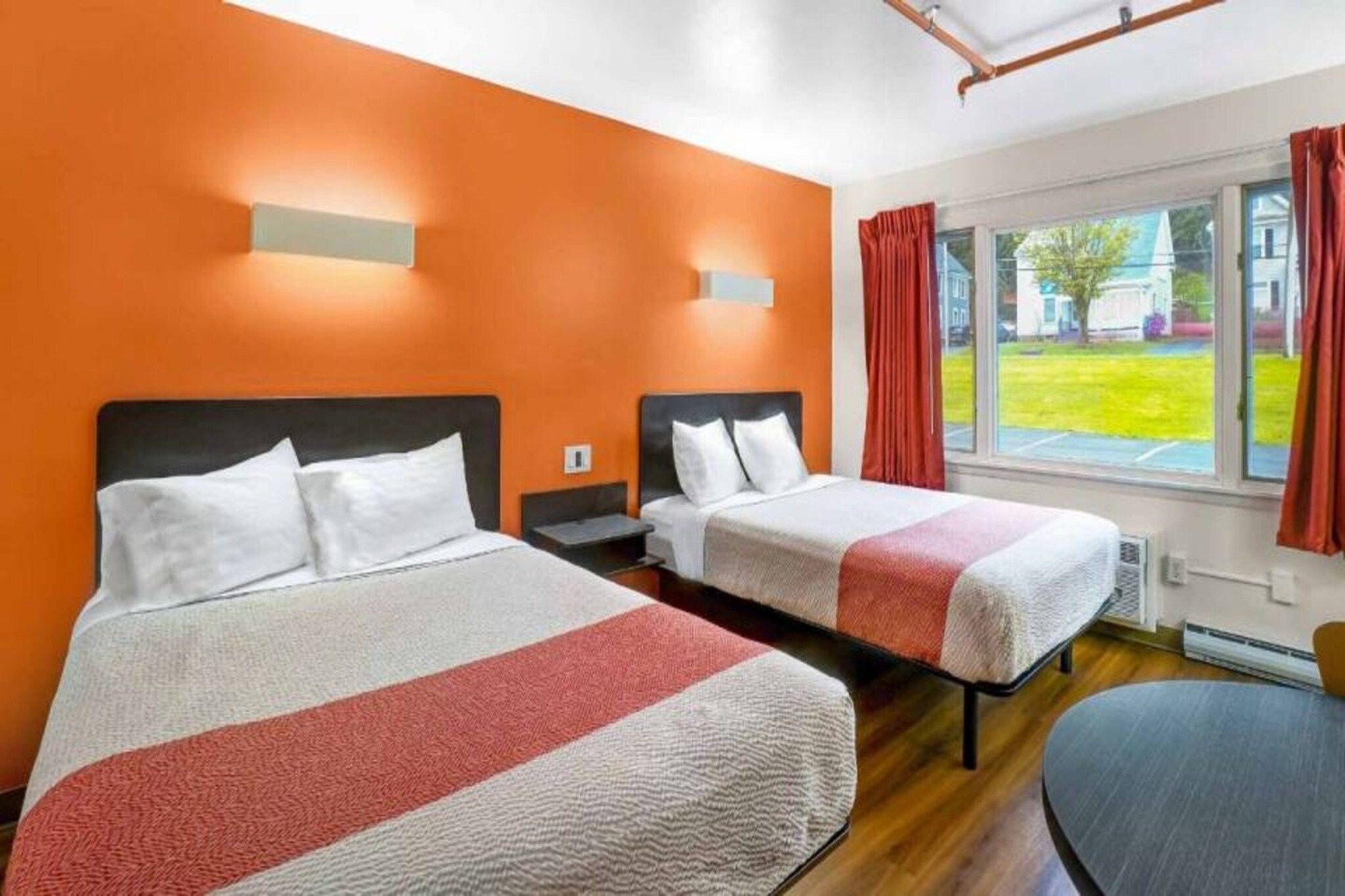 A hotel room with two beds, a window with curtains, and a view of the outside.