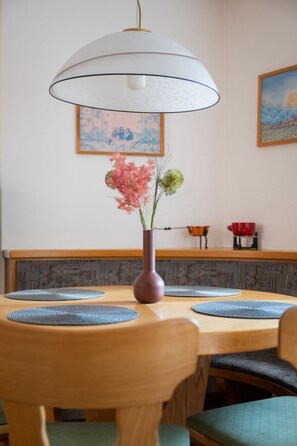 Een eettafel met placemats, een vaas met bloemen en een hanglamp.