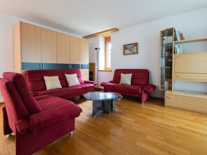 A modern living room with two red sofas, a glass coffee table, wooden flooring, and a bookshelf. - Skistrasse 8B Appartement/Fewo, Dusche oder Bad, WC 3½-Zimmerwohnung by Interhome (Davos)