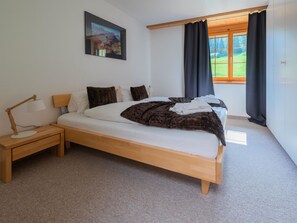 A bedroom with a wooden bed, a nightstand, a desk, a window with curtains, and a painting on the wall. - Skistrasse 8B Appartement/Fewo, Dusche oder Bad, WC 3½-Zimmerwohnung by Interhome (Davos)