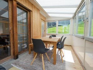 A room with a wooden table and chairs, a large window with a view of greenery, and a sliding glass door. - Skistrasse 8B Appartement/Fewo, Dusche oder Bad, WC 3½-Zimmerwohnung by Interhome (Davos)
