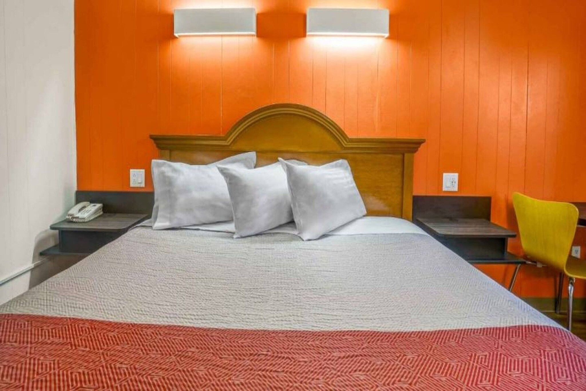 A hotel room with a bed, two bedside tables, a telephone, a chair, and a wall-mounted light fixture.