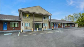 A motel with a central building and attached units, a parking lot, and a clear sky.