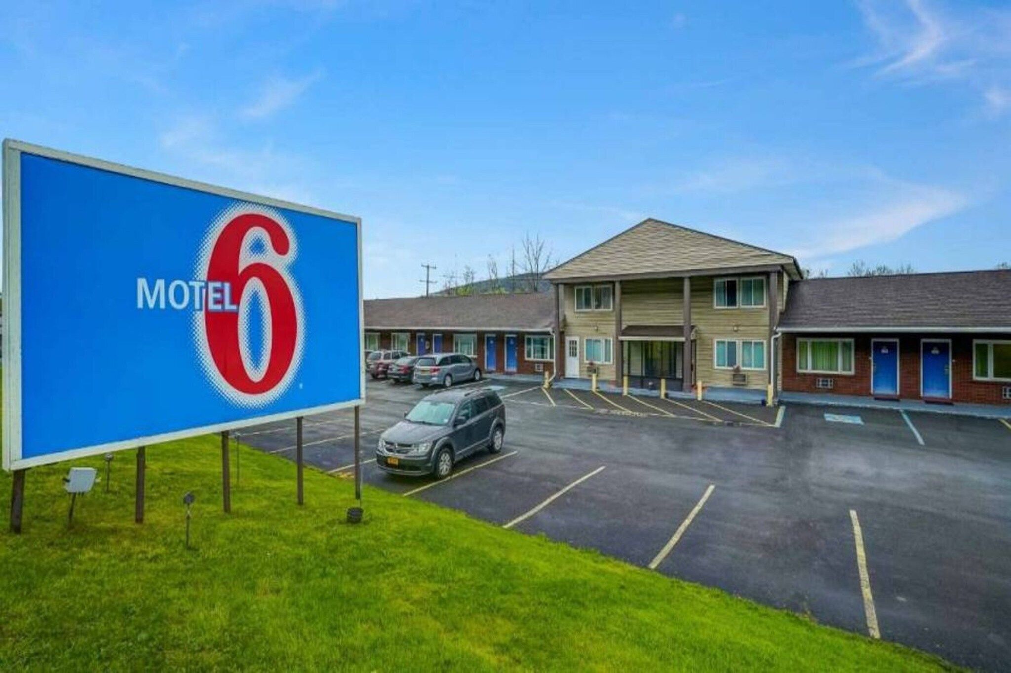 A motel with a large sign, a parking lot, and a building with multiple rooms.