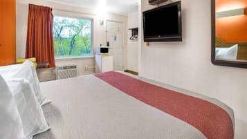 Een hotelkamer met een bed, een televisie, een bureau en een raam met gordijnen.