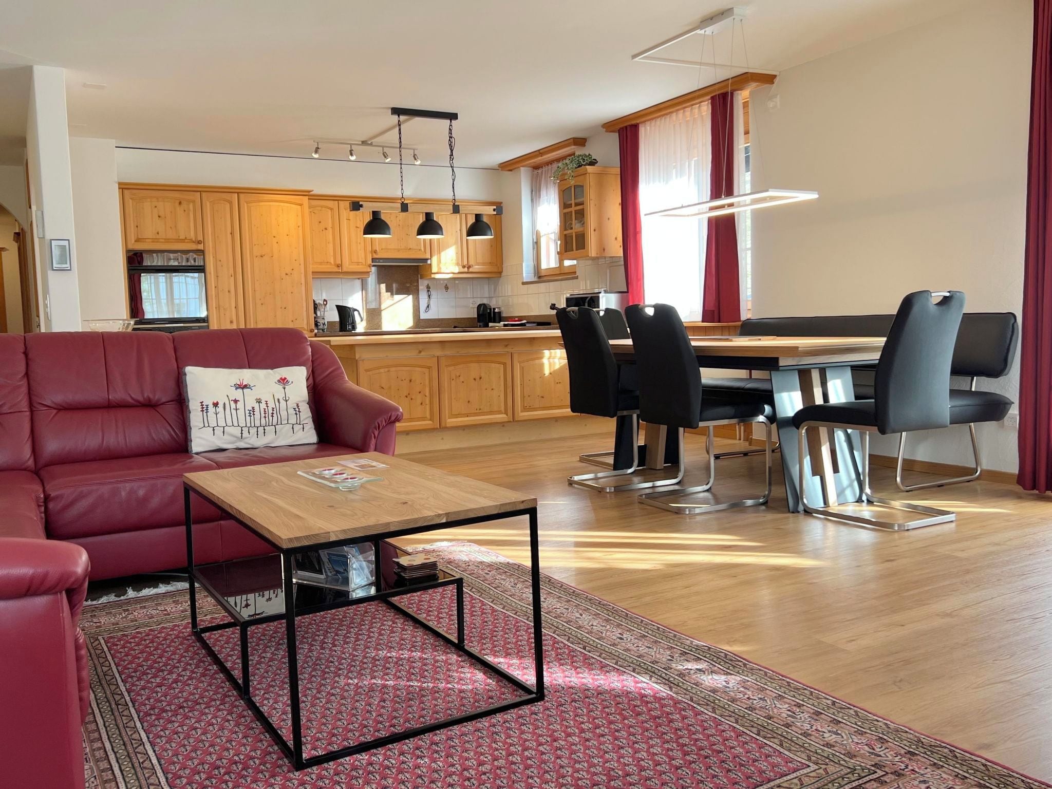 A modern living room with a red sofa, a wooden coffee table, and a dining area with a table and chairs.