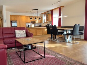Un salon moderne avec un canapé rouge, une table basse en bois et un coin repas comprenant une table et des chaises.