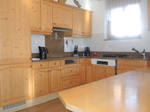 A kitchen with wooden cabinets, a built-in oven, a sink, and a window with curtains. - Bünda Residenz 101 Appartement/Fewo, Dusche oder Bad, WC 4½-Zimmerwohnung by Interhome (Davos)