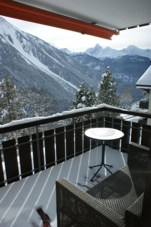 Un balcón con mesa y sillas, con vistas a un paisaje montañoso nevado.