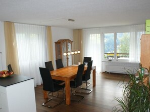 A dining area with a wooden table, black chairs, a fruit bowl, a clock, and a window with a view of trees. - Clematis 1 Appartement/Fewo, Dusche oder Bad, WC 3½-Zimmerwohnung by Interhome (Wiesen)